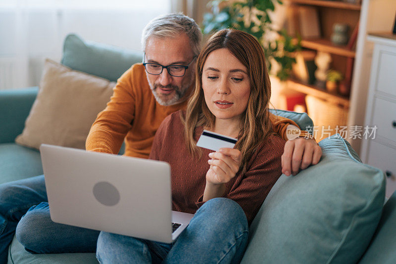 husband and wife sitting on couch and using laptop and internet card.